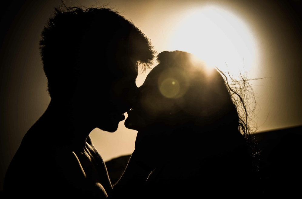 Two people being intimate and kissing, illuminated by sunlight.