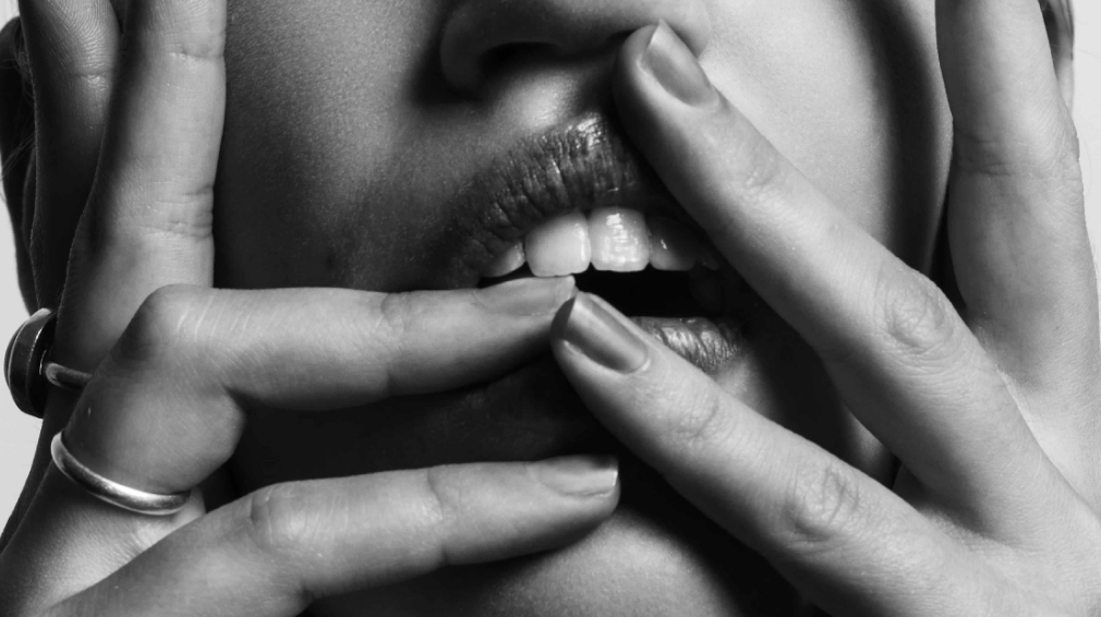 A female escort holding her face sensually, focusing on her mouth and fingers.